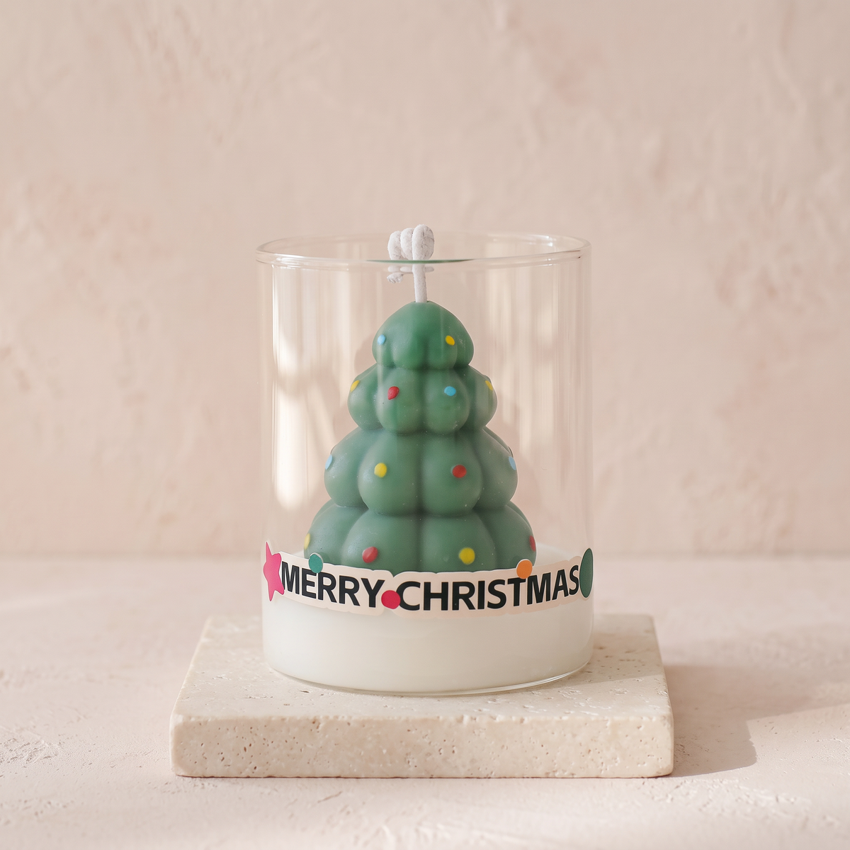Green Christmas tree scented candle in a clear glass cup with a Merry Christmas band